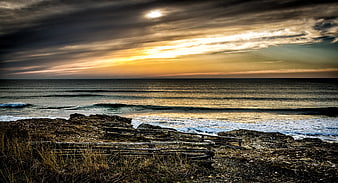 Dramatic Sunset Over Rocky Coastline with Wooden Fence