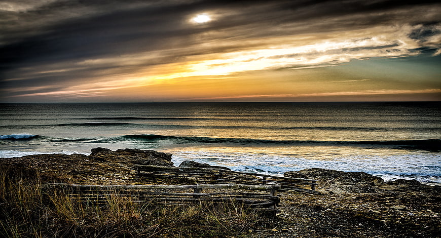 Dramatic Sunset Over Rocky Coastline with Wooden Fence