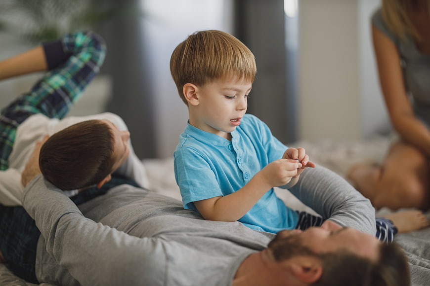 Father and son playing on bed with family