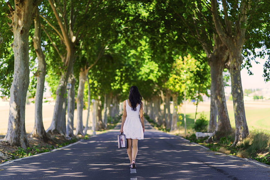 Woman in White Dress Walking Down Tree-Lined Road
