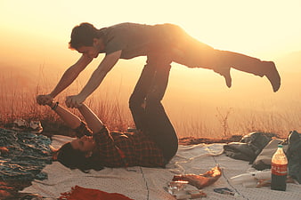 Couple playing acrobatics on picnic blanket at sunset