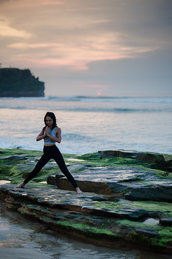 Woman practicing yoga on mossy rocks at sunset