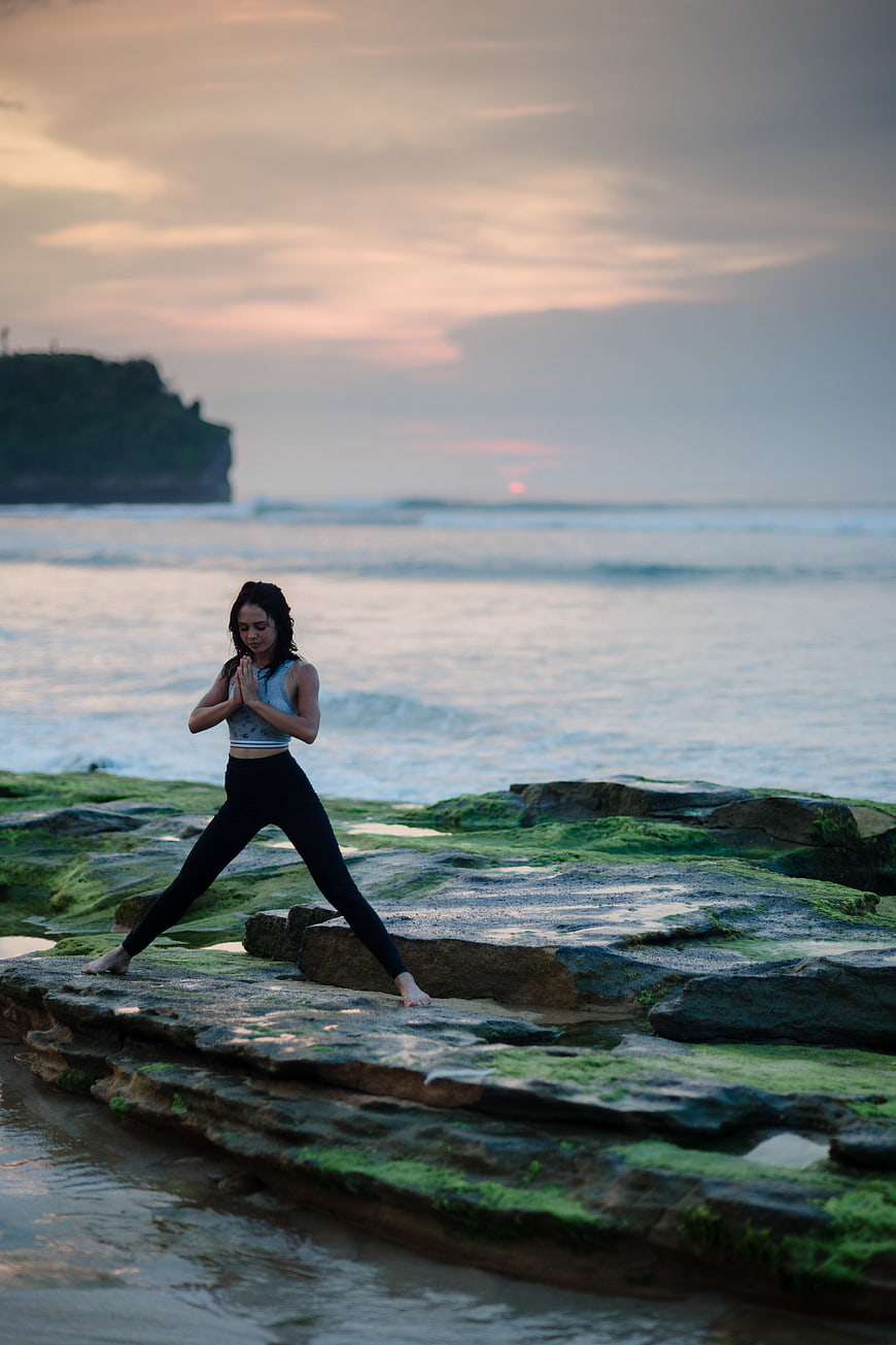 Woman practicing yoga on mossy rocks at sunset