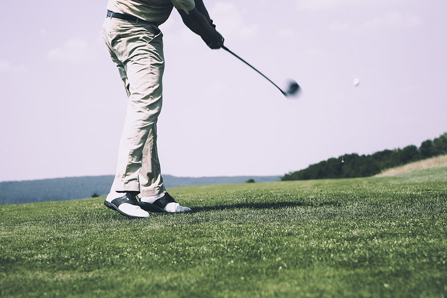 Golfer Swinging Club on Green Fairway