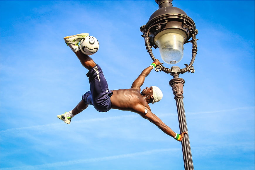 Athletic man performing acrobatic soccer move on lamp post