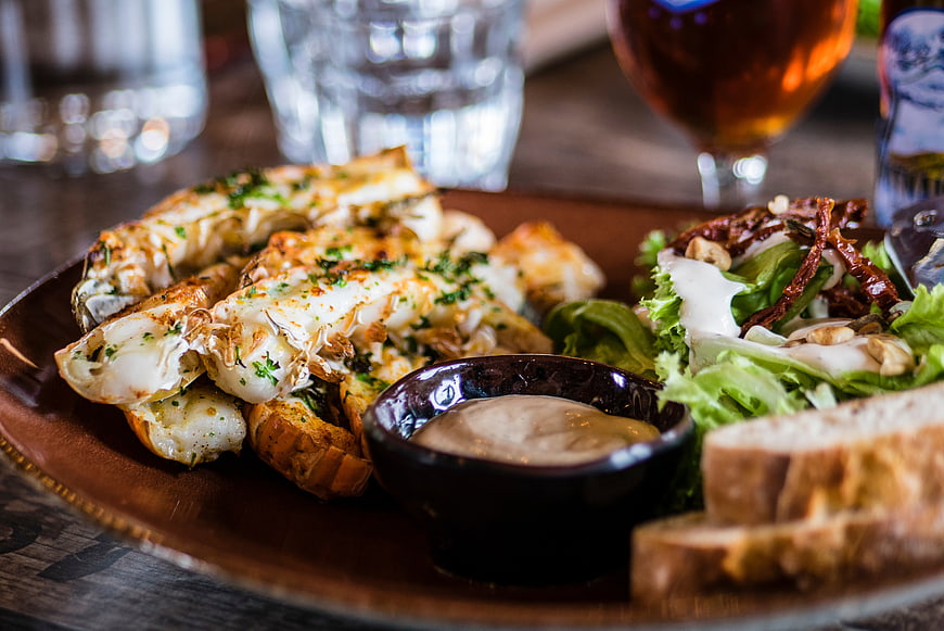 Grilled lobster tail with salad and dipping sauce on wooden plate