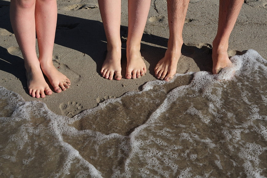 Family Feet Standing On Wet Sand At Beach Shoreline