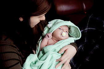 Mother holding newborn baby wrapped in green hooded towel