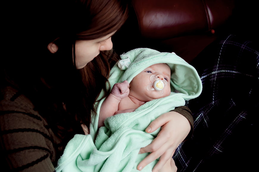 Mother holding newborn baby wrapped in green hooded towel