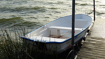 White rowboat docked at wooden pier on choppy lake