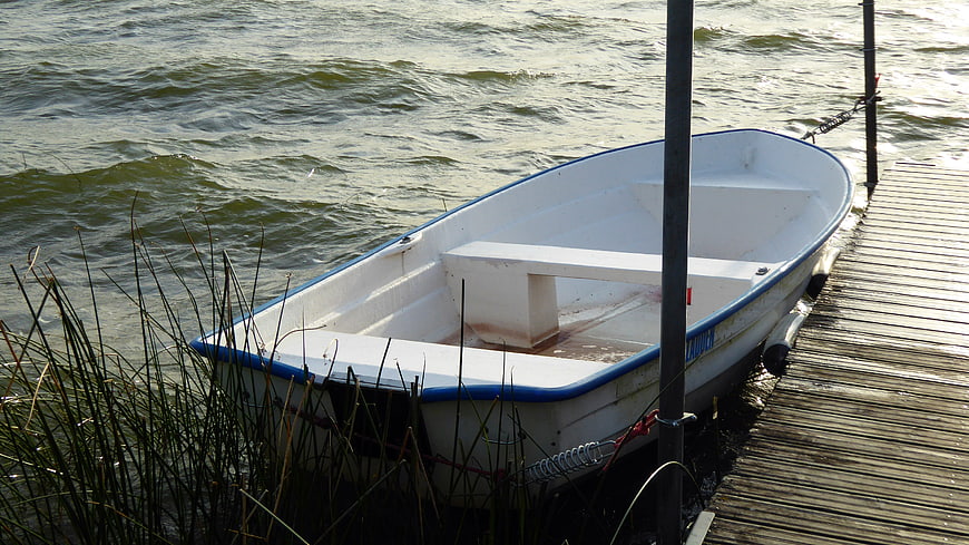 White rowboat docked at wooden pier on choppy lake