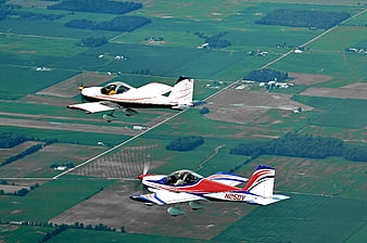 Two Light Sport Aircraft Flying In Formation Over Green Farmland