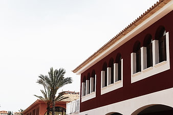 Red and white Mediterranean building with arched windows and palm tree
