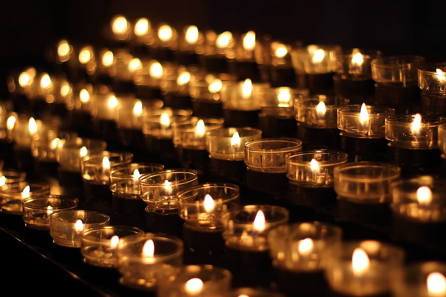 Rows of lit tea light candles in a dark church setting
