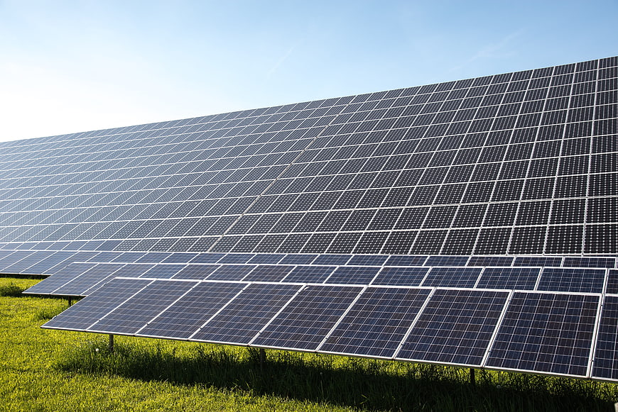 Large Solar Panel Array In Green Field Under Blue Sky