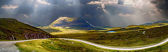 Panoramic mountain landscape with winding road and dramatic sunbeams