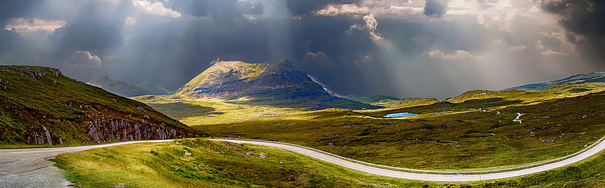 Panoramic mountain landscape with winding road and dramatic sunbeams