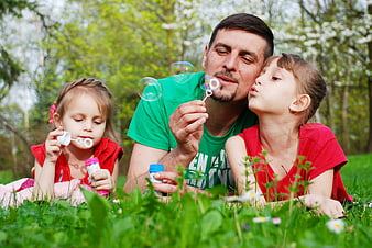 Father and two daughters blowing soap bubbles in a park