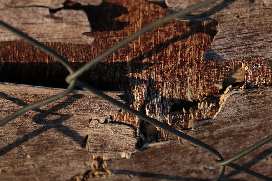 Close-up of weathered wood texture with wire fence shadows