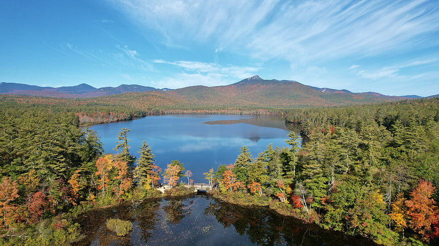 Aerial View of Serene Lake Surrounded by Autumn Forest and Mountains