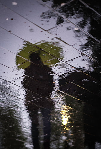 Silhouette of person with umbrella reflected in rain puddle
