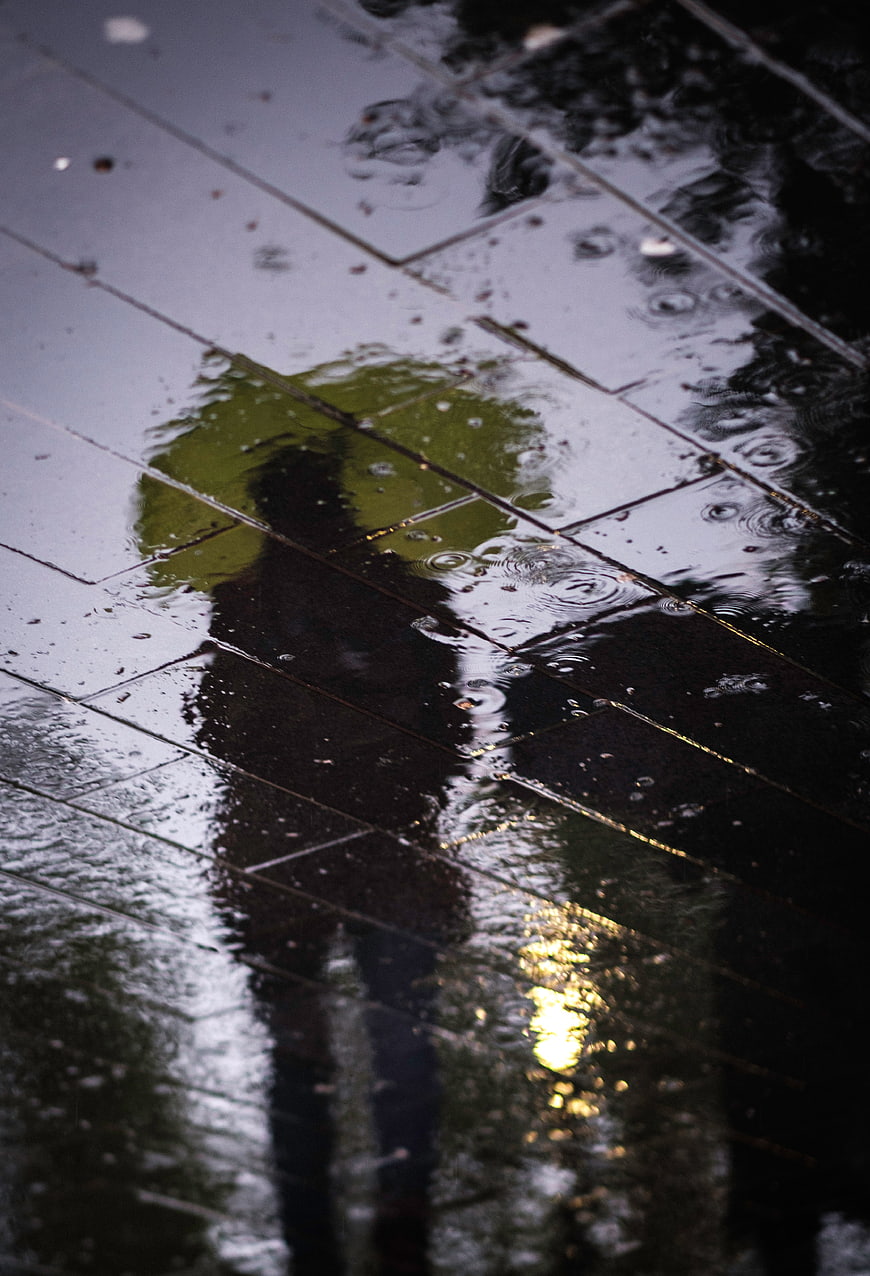 Silhouette of person with umbrella reflected in rain puddle