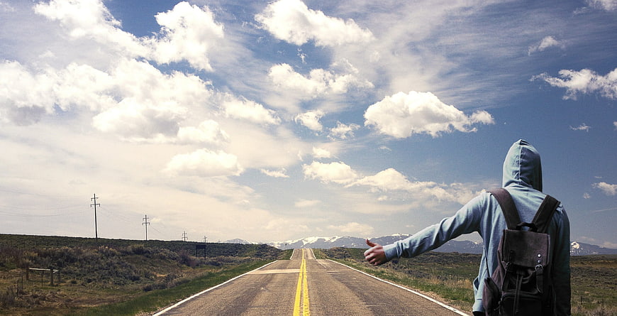 Hitchhiker on Country Road with Backpack and Mountains