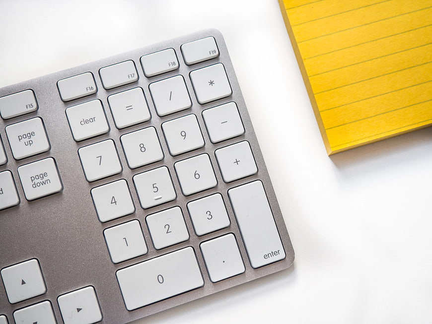 Silver Keyboard and Yellow Notepad on White Desk