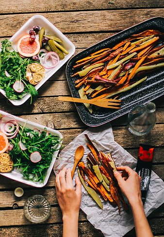 Top view of roasted sweet potato fries and fresh salad on wooden table