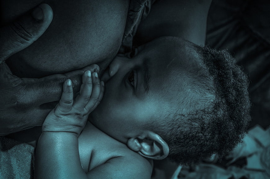 Close-up of African baby breastfeeding with mother's hand