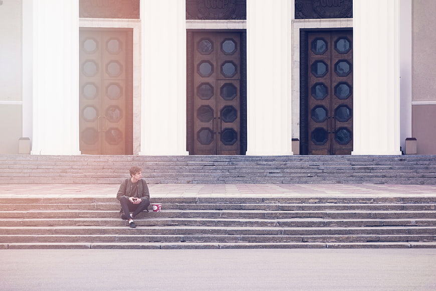 Man sitting on steps of grand building with light leak effect