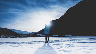 Woman standing in snow facing sun and mountains