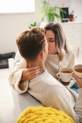 Young couple kissing on sofa with coffee mugs