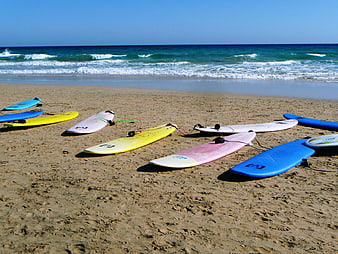 Colorful surfboards lined up on sandy beach with ocean waves