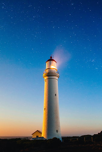 Illuminated white lighthouse against a starry night sky