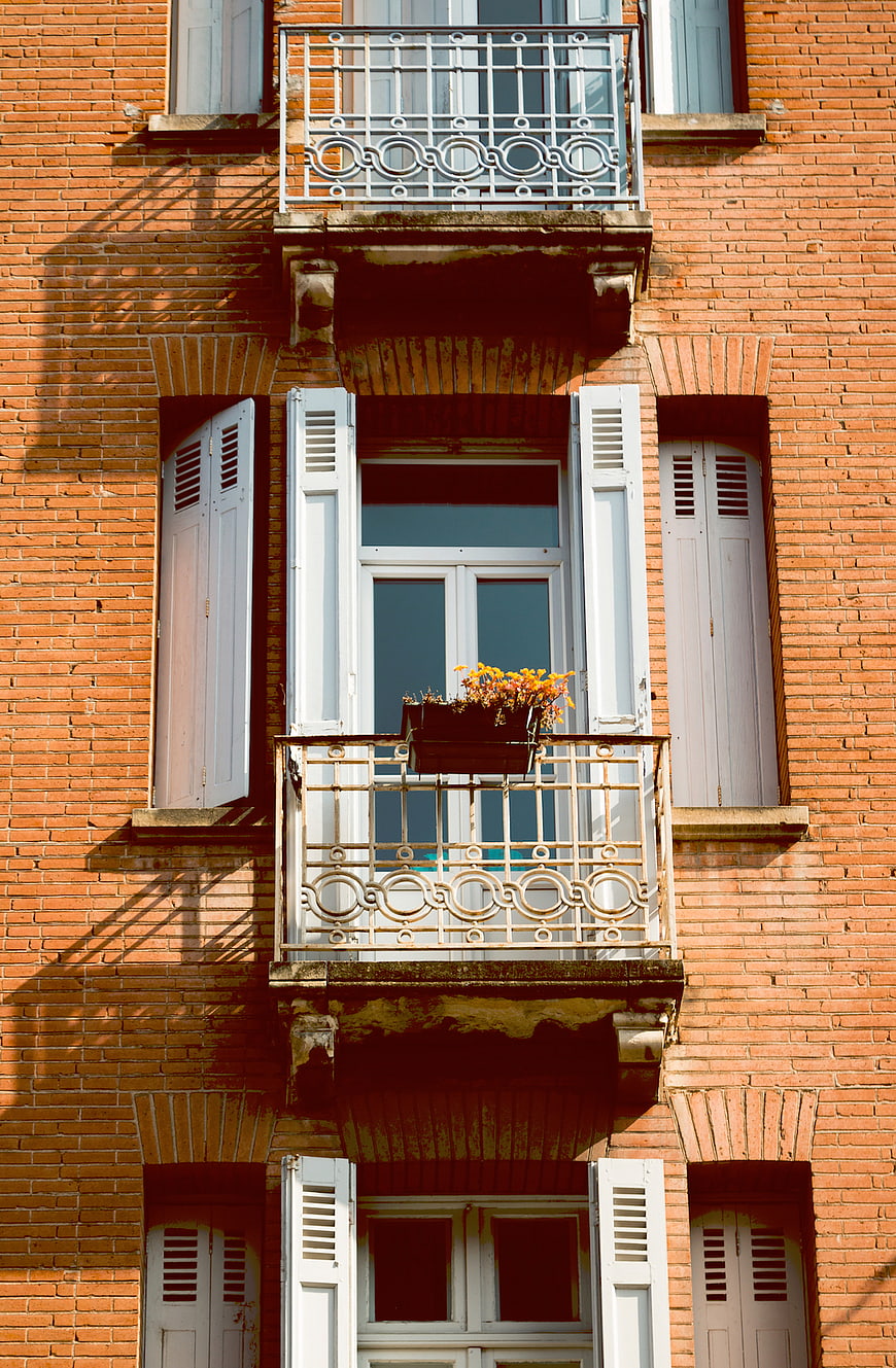 Red Brick Building Facade with White Shutters and Balcony
