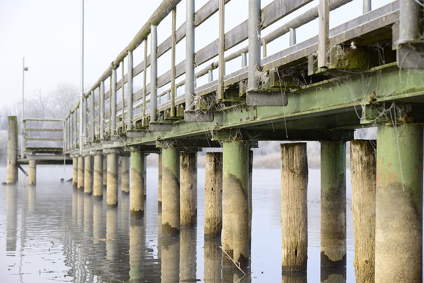 Weathered wooden pier with cobwebs over calm winter water