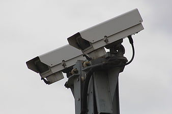 Two white CCTV surveillance cameras mounted on a metal pole against a gray sky
