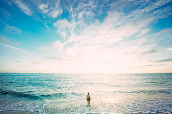 Woman standing in ocean waves facing bright sky