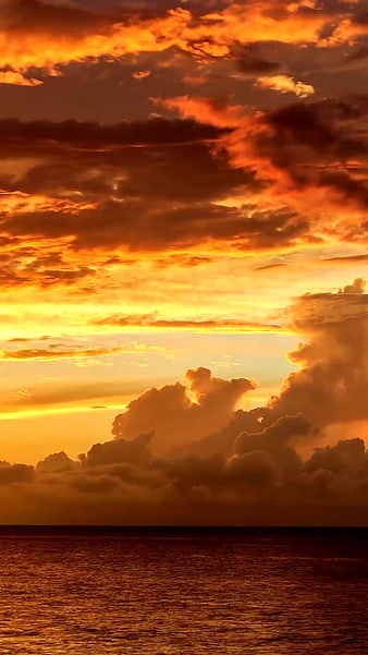 Dramatic fiery orange sunset over ocean with clouds