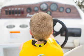 Young boy in yellow life jacket steering a boat