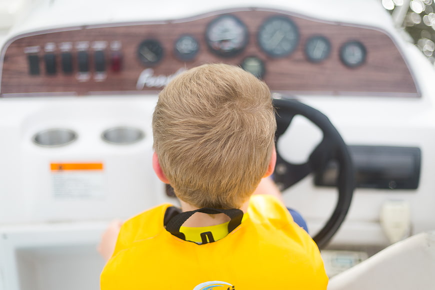 Young boy in yellow life jacket steering a boat