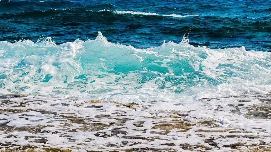 Turquoise ocean waves crashing on rocky shore with white foam