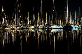 Night view of sailboat masts reflecting in calm harbor water