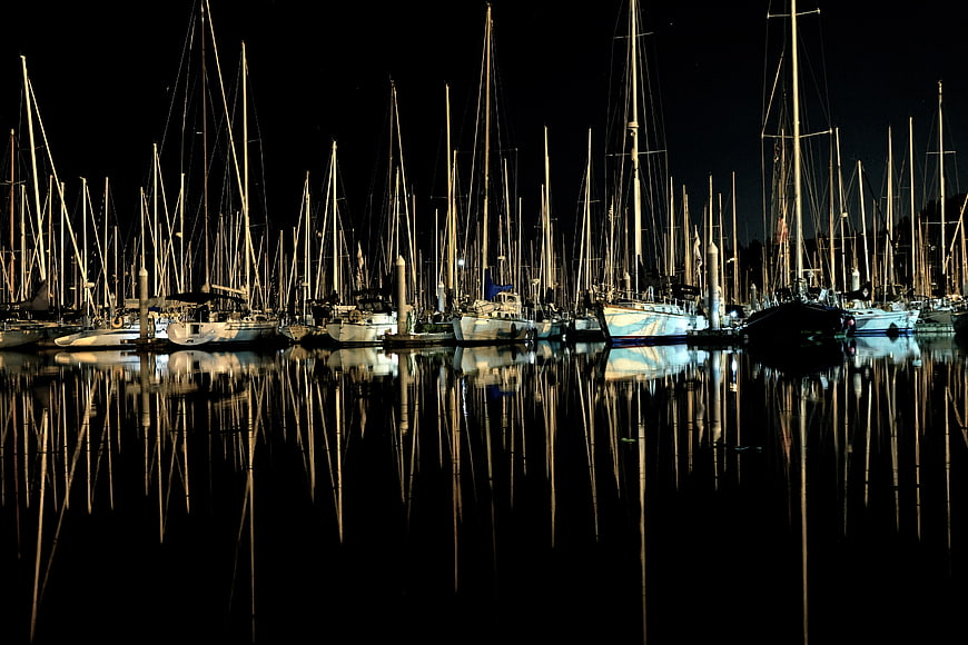 Night view of sailboat masts reflecting in calm harbor water