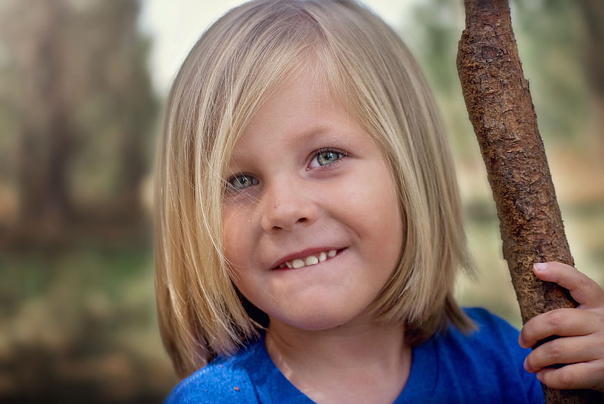 Close-up portrait of smiling blonde child holding stick outdoors