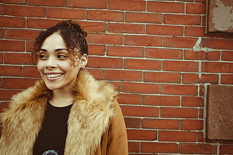 Smiling woman in fur coat against red brick wall