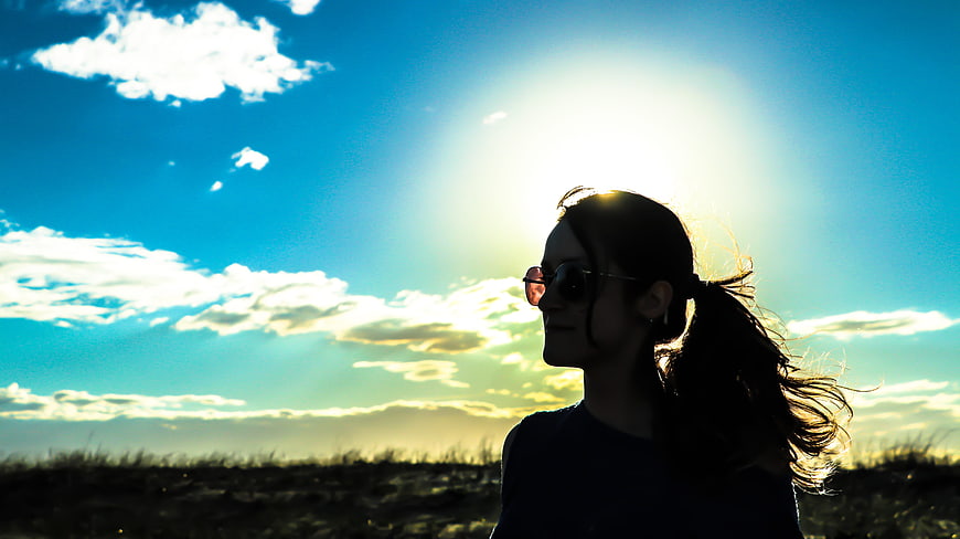 Silhouette of Woman with Sunglasses Against Bright Sun and Blue Sky