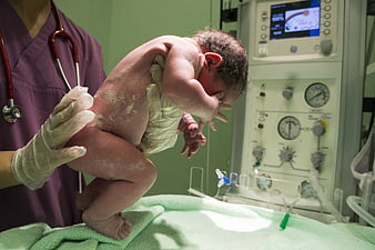 Newborn baby held by nurse in hospital delivery room