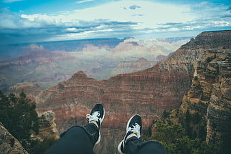 First-person view of sneakers dangling over a vast canyon landscape